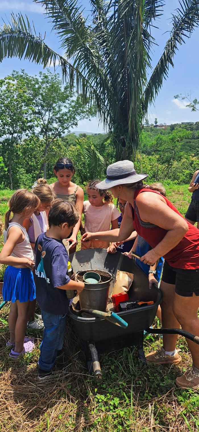 Children gathered around a teacher examining soil and seedlings